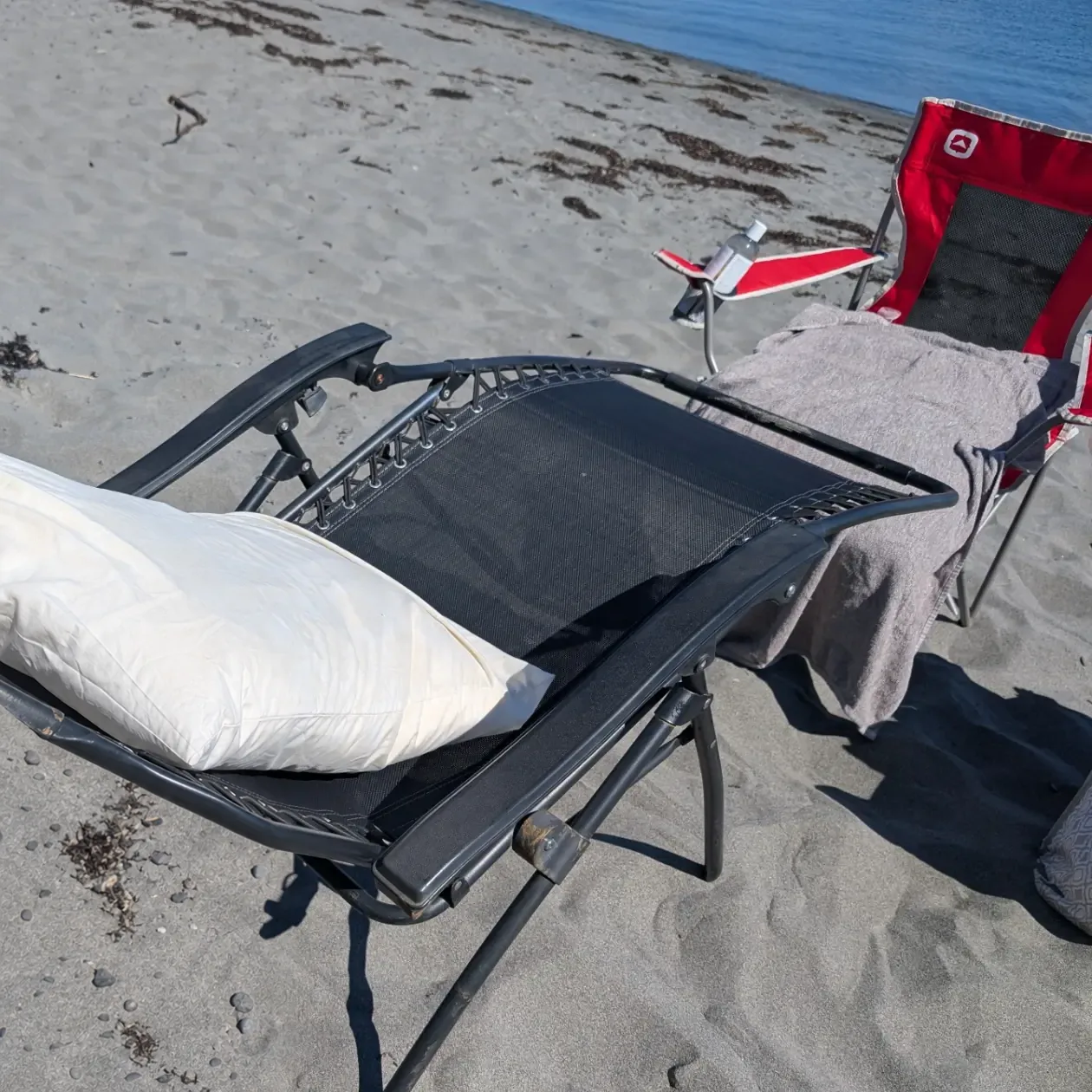 Camp chairs and a pillow set up on the sand at the water's edge, ready for a beach reflexology session