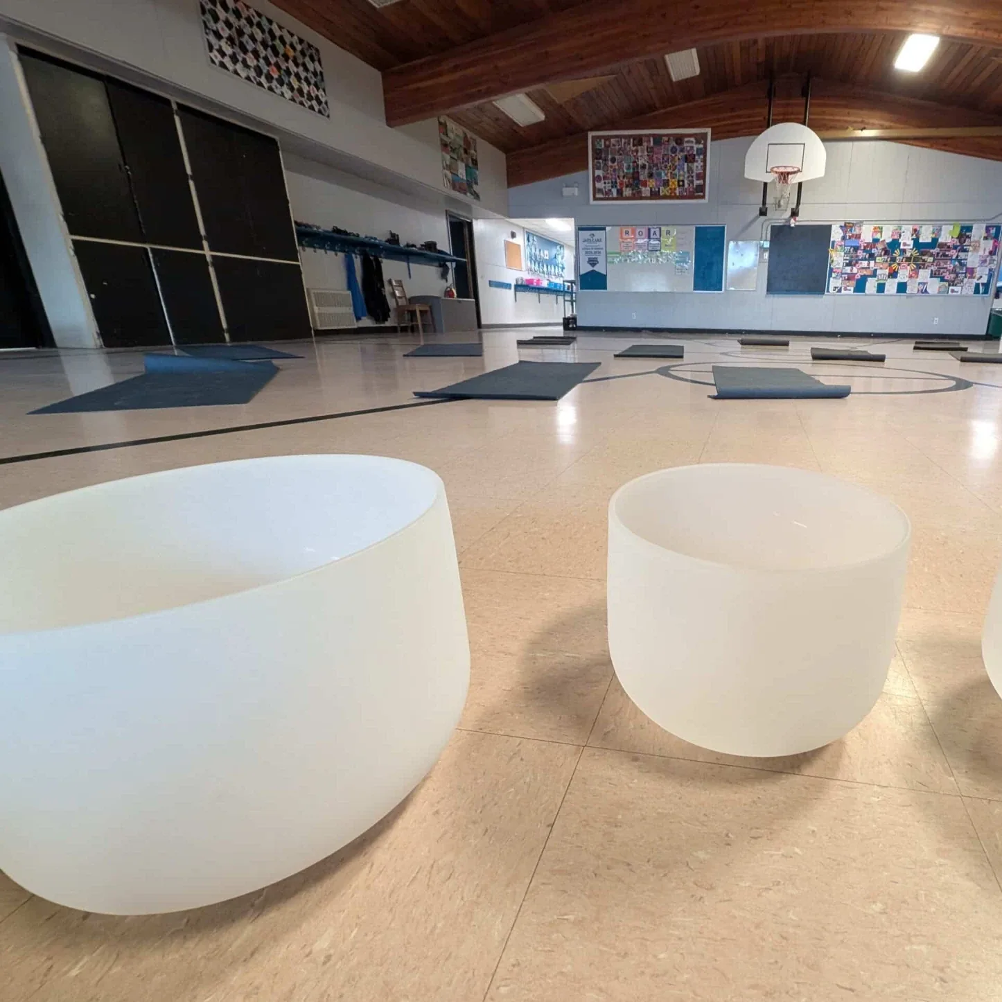 Three crystal singing bowls set out on the floor in front of rolled yoga mats, ready for a group sound bath